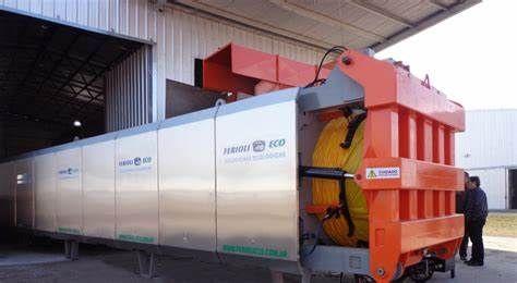 Large industrial machine partially inside a warehouse with metallic exterior and visible orange components.