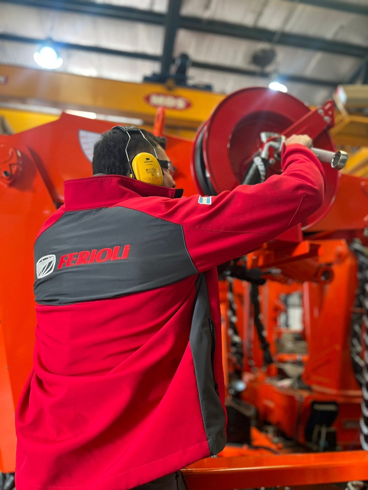 Person in red jacket with ear protection operating industrial machinery indoors.