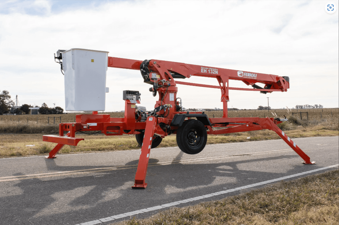 Red mobile aerial platform on a road with stabilizing legs extended.